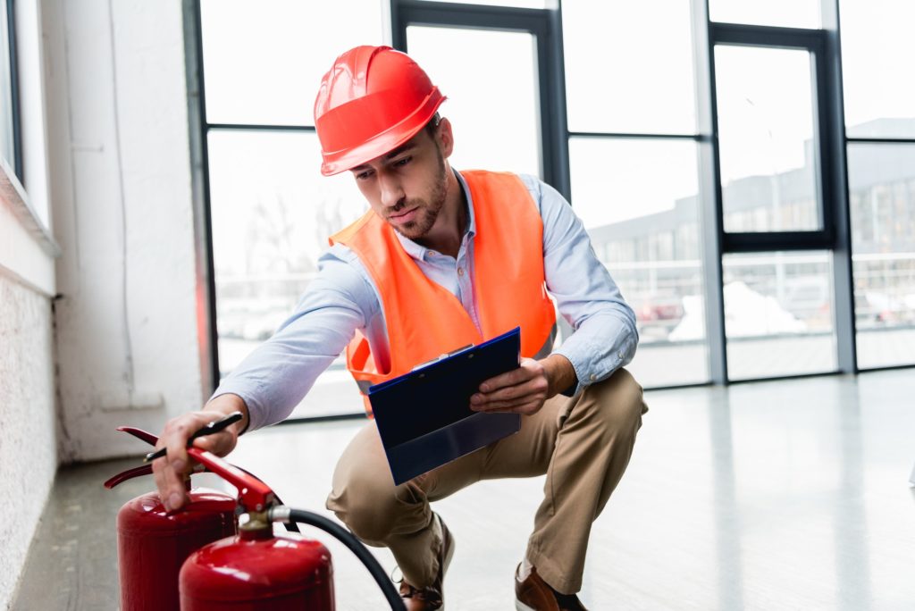 serious fireman in helmet checking extinguishers while sitting with clipboard